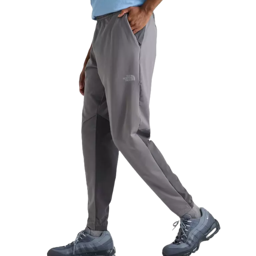 Gray track pants from The North Face featuring a relaxed fit, elastic waistband, ankle cuffs, and side pockets, paired with gray-blue athletic shoes.