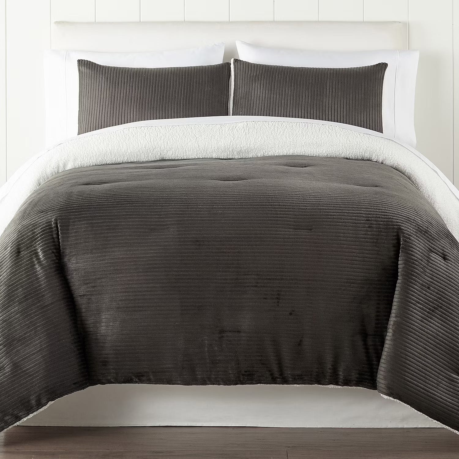 A bed with white sheets topped with a textured dark gray coverlet and matching pillows.