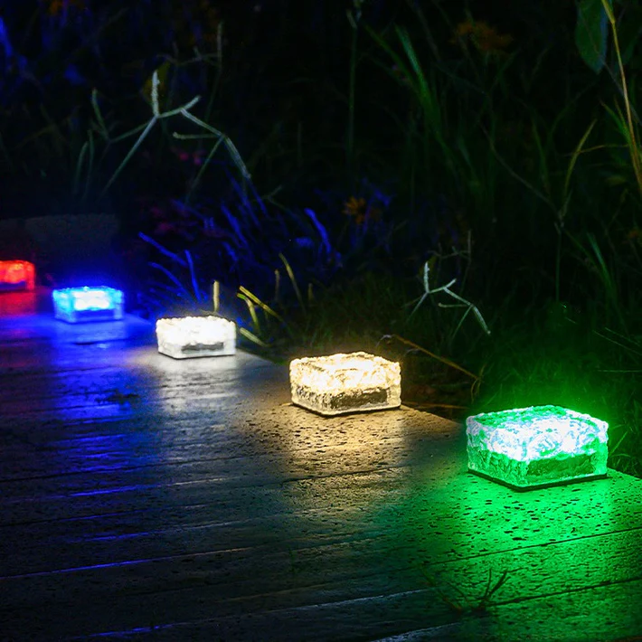 6pk Solar Ice Brick Lights are colorful, cube-shaped lights designed for outdoor pathways, featuring green, white, blue, and red hues that illuminate the ground at night, creating a decorative and functional walkway.