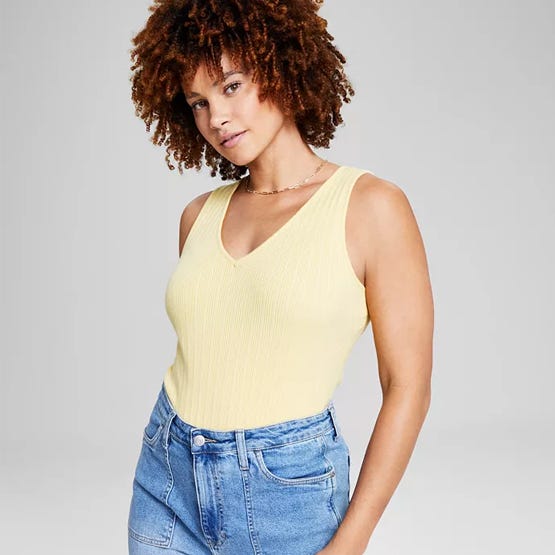 A woman wearing a yellow ribbed tank top and blue high-waisted jeans.