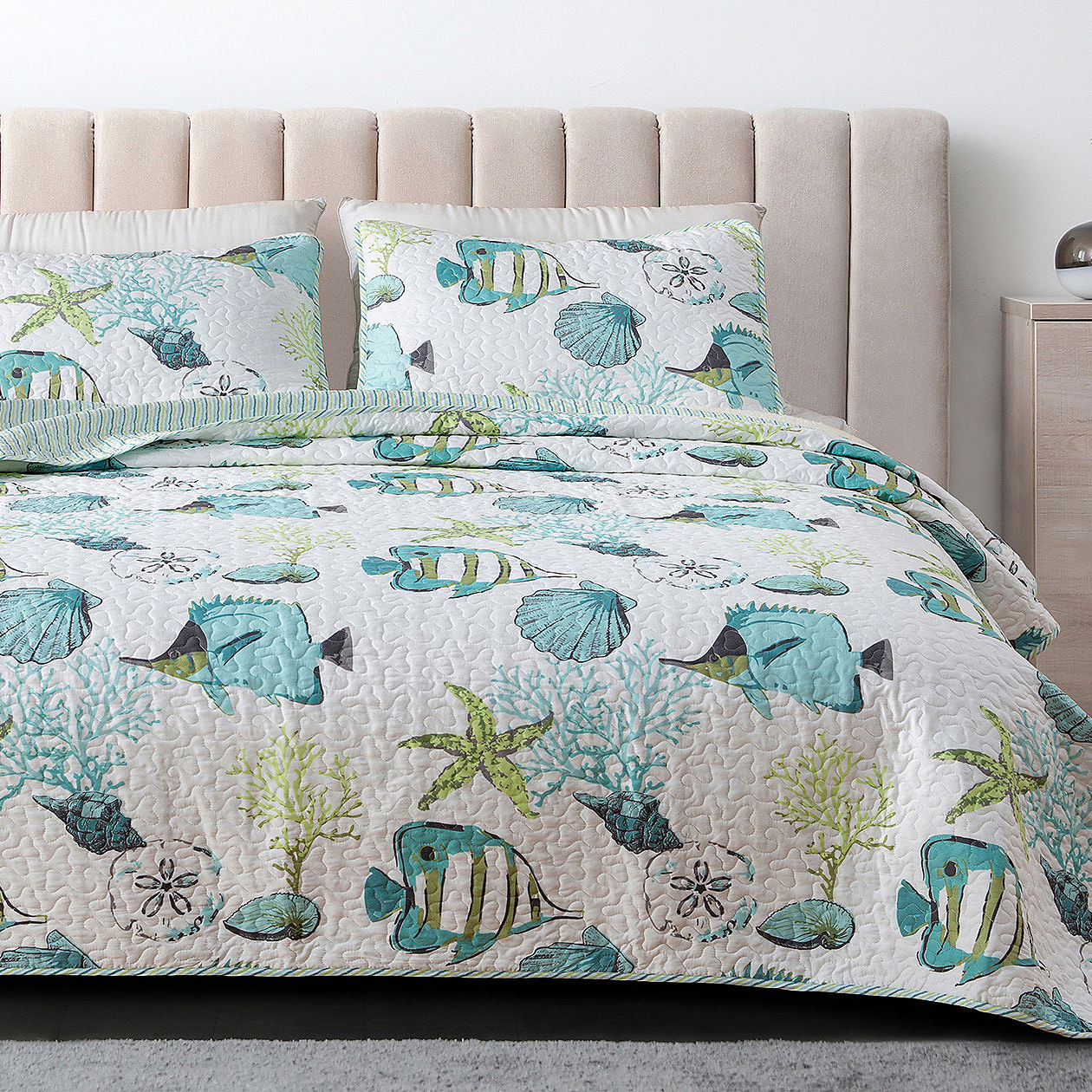 A quilt and pillow shams with a marine life pattern, including various fish, coral, and seaweed designs in shades of blue and green.