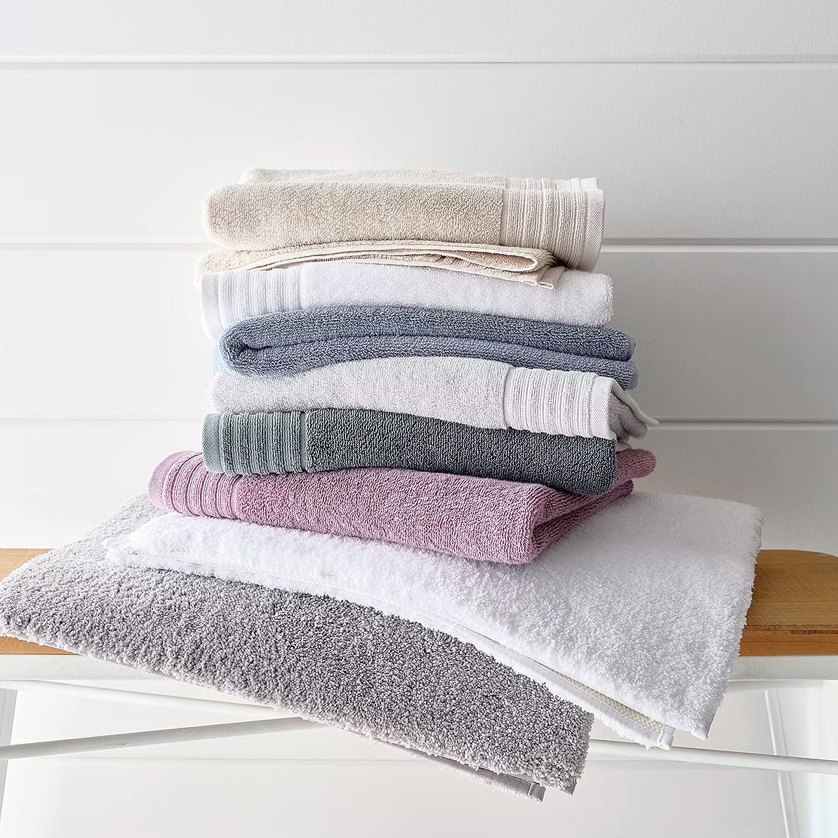 A stack of folded towels in various colors, including beige, white, blue, green, pink, and gray, arranged on a shelf.