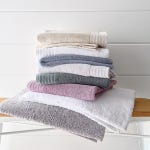 A stack of folded towels in various colors, including beige, white, blue, green, pink, and gray, arranged on a shelf.