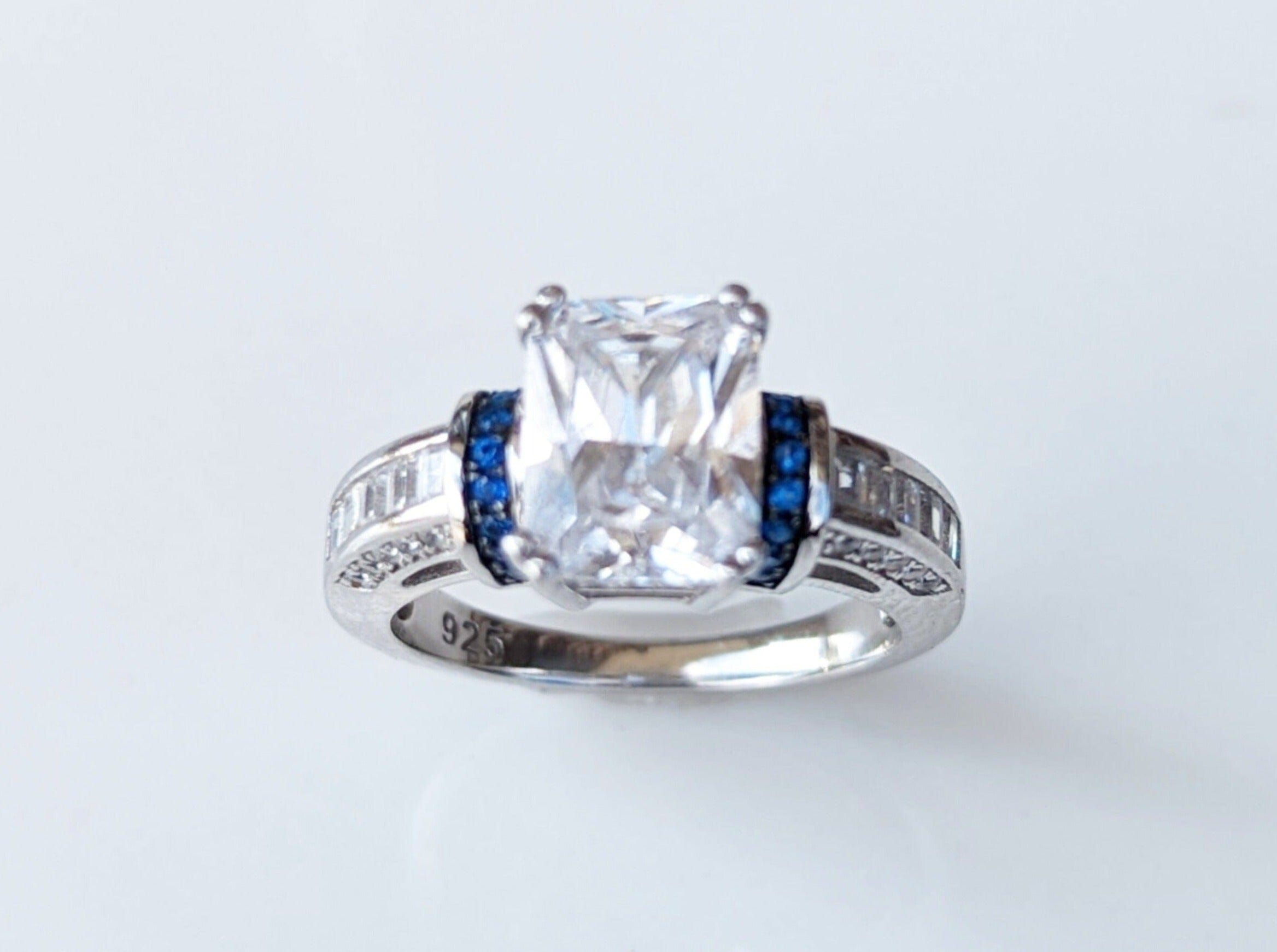 Silver ring with a large central diamond and smaller blue gemstones on the sides.