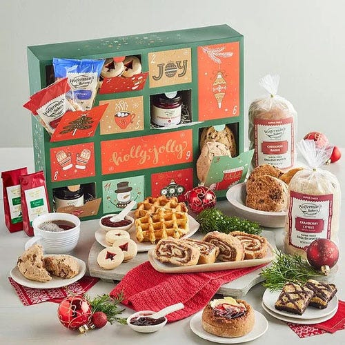 An advent calendar-style box with Christmas-themed packaging contains items like waffles, cinnamon rolls, bread, and cookies, alongside festive decorations and small packaged goods.