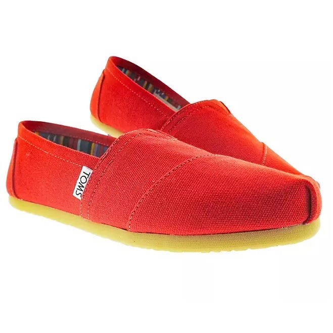 A pair of red canvas slip-on shoes with white labels on the sides.