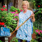 A woman is holding Grandpa's Weeder, a long-handled gardening tool with a four-claw steel head.