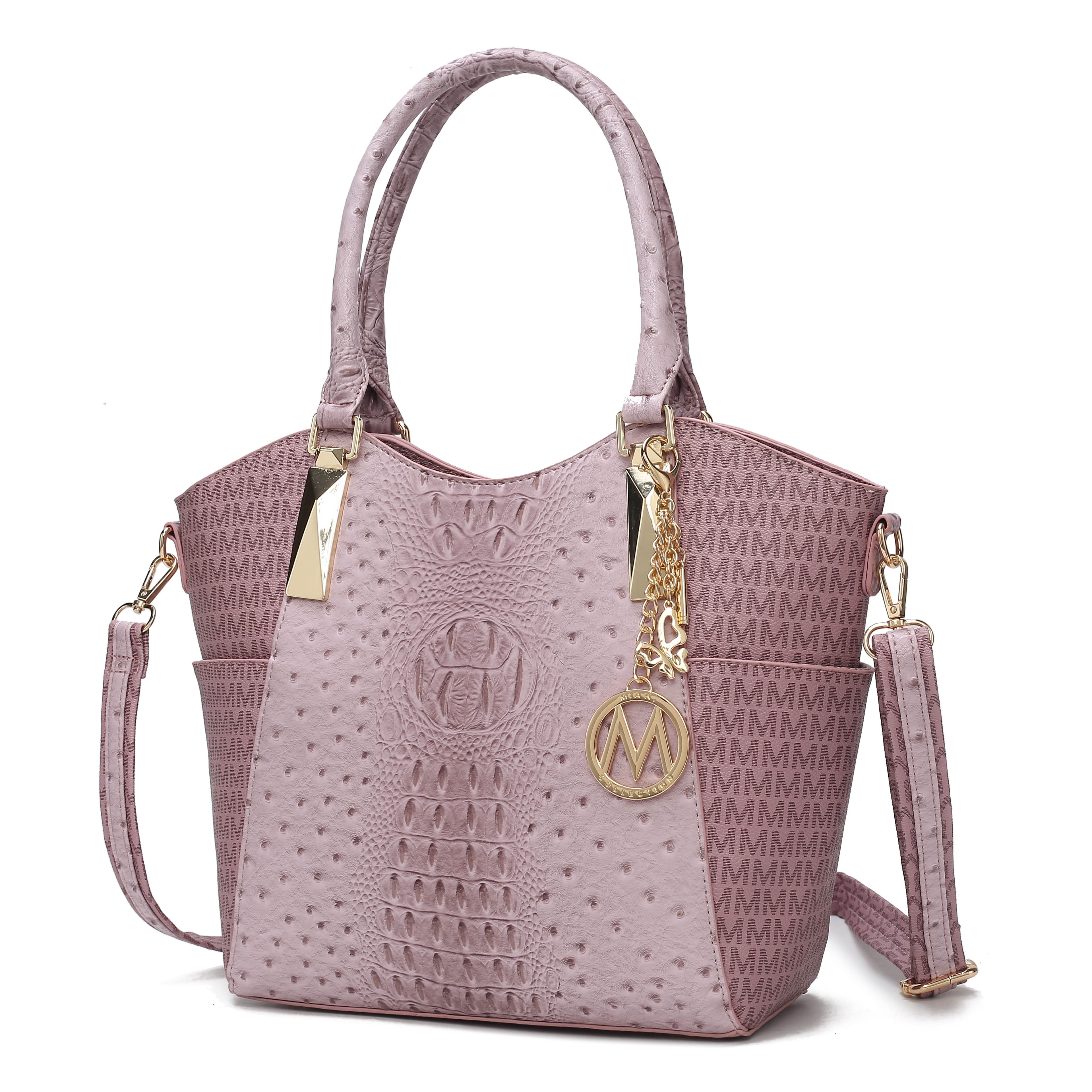 The MKF Kristal Signature Tote features a mauve color with a textured design and includes gold-tone hardware, a detachable shoulder strap, and an \“M\“ charm. Its sides display repeated \“M\“ patterns for a stylish look.