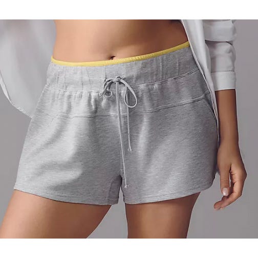 A person is wearing gray drawstring shorts with a yellow waistband, paired with a white outer garment.