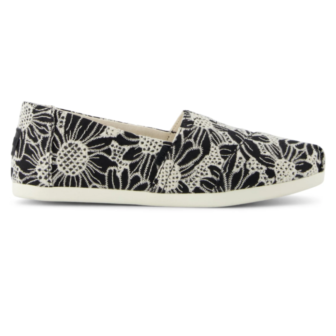 Slip-on canvas shoe with a black and white floral lace pattern and a white rubber sole.