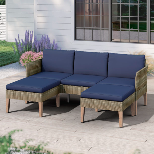 A wicker outdoor sectional sofa with navy blue cushions and coordinating ottoman on a patio.