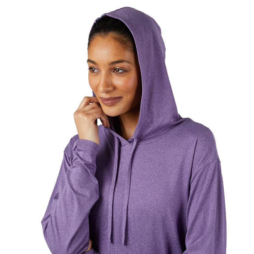 A person wearing a purple hoodie with the hood up, smiling with a contemplative expression.