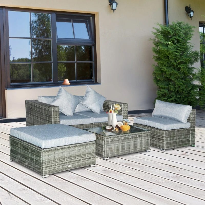 A rattan patio furniture set with cushions, including two armchairs, an ottoman, and a glass-topped coffee table.