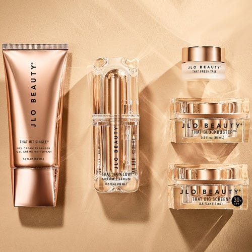 JLo Beauty skincare products including a cleanser tube, serum bottle, and jars of cream with SPF protection.
