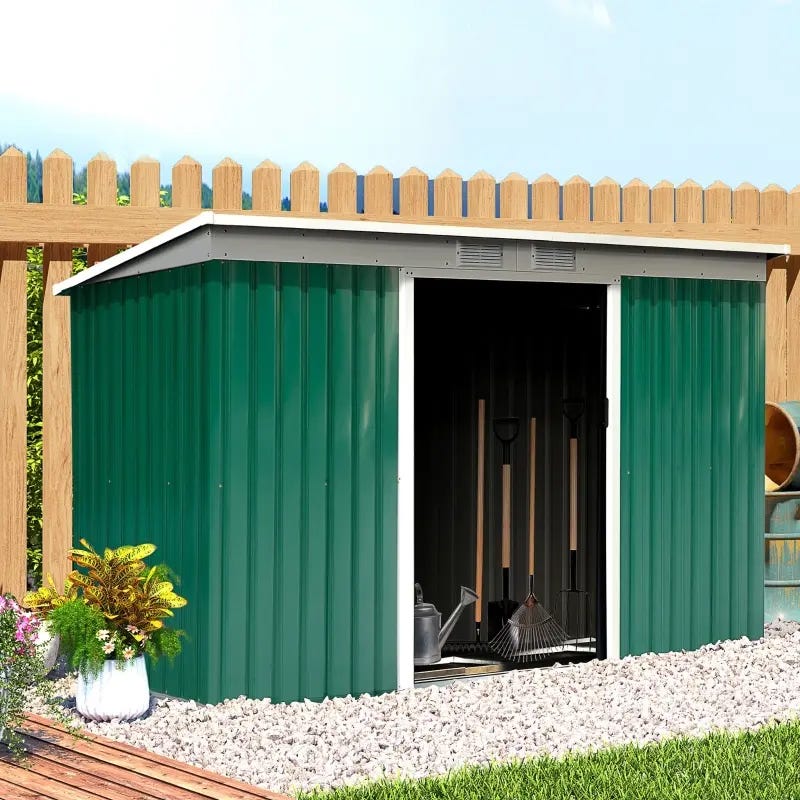 Green metal garden shed with open doors revealing garden tools inside, placed next to a wooden fence and plants.