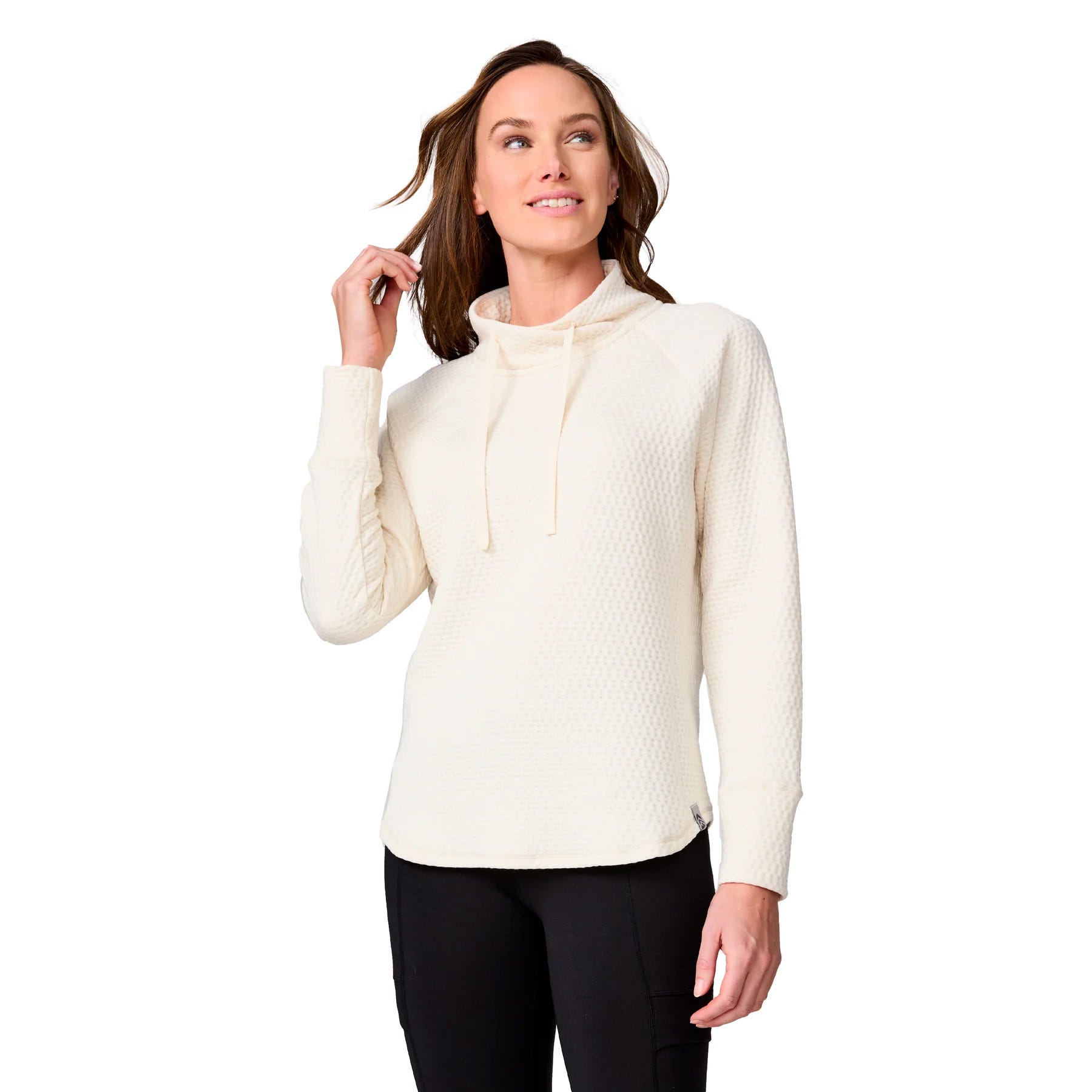A woman is wearing a textured, cream-colored pullover sweater with a cowl neck and drawstrings, paired with black pants.