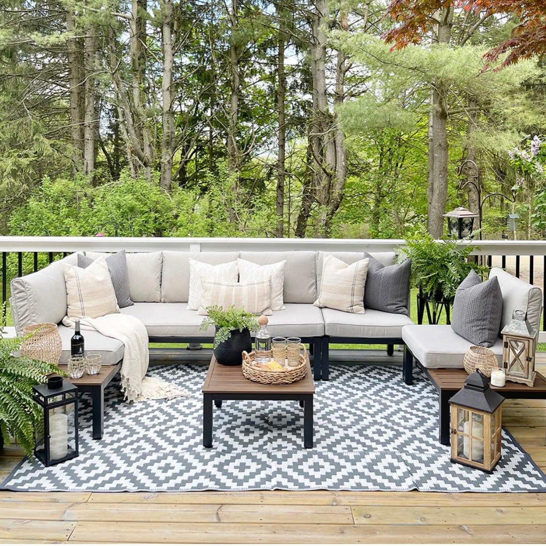 Outdoor patio setup with sectional sofa, patterned rug, two small tables, and decorative lanterns.