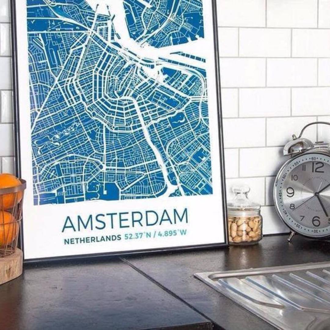 A framed map print of Amsterdam, a silver analog clock, and a glass jar of peanuts on a kitchen countertop.