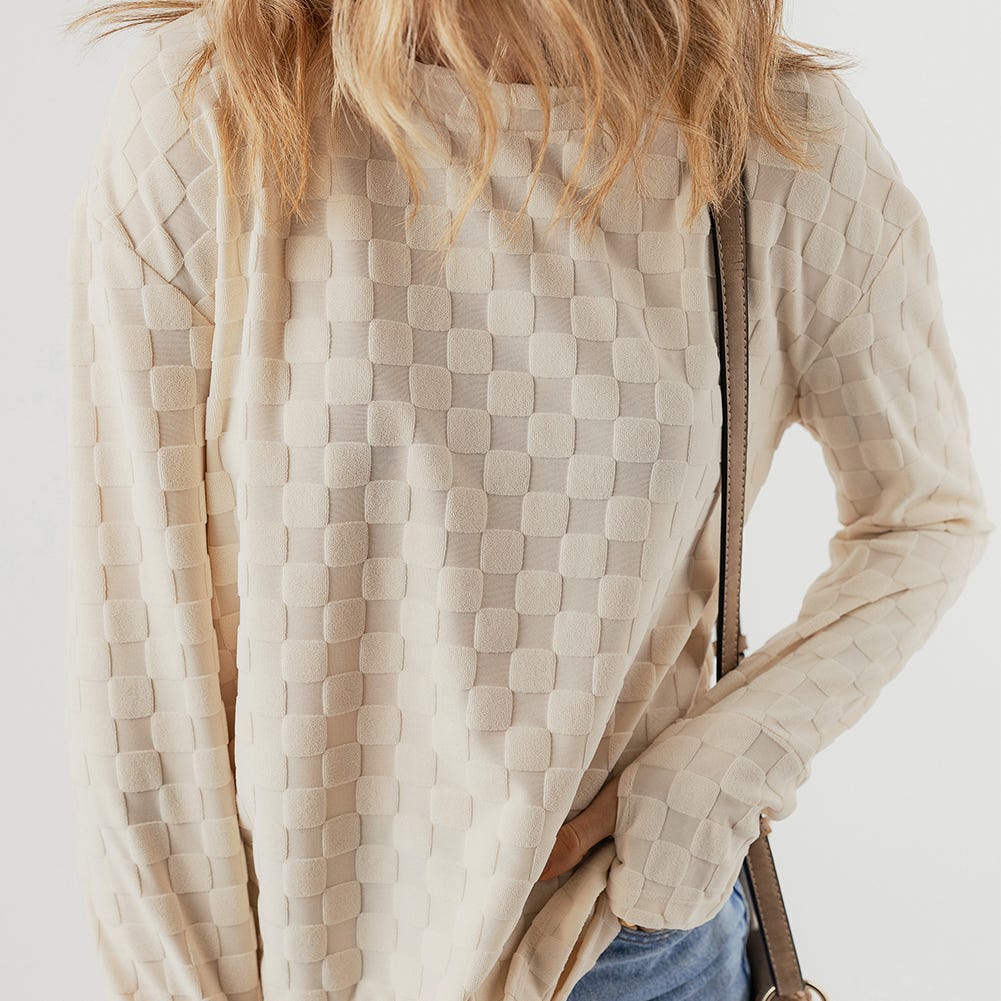 Beige textured jacket with square pattern design and visible zipper, paired with jeans and a shoulder bag strap.