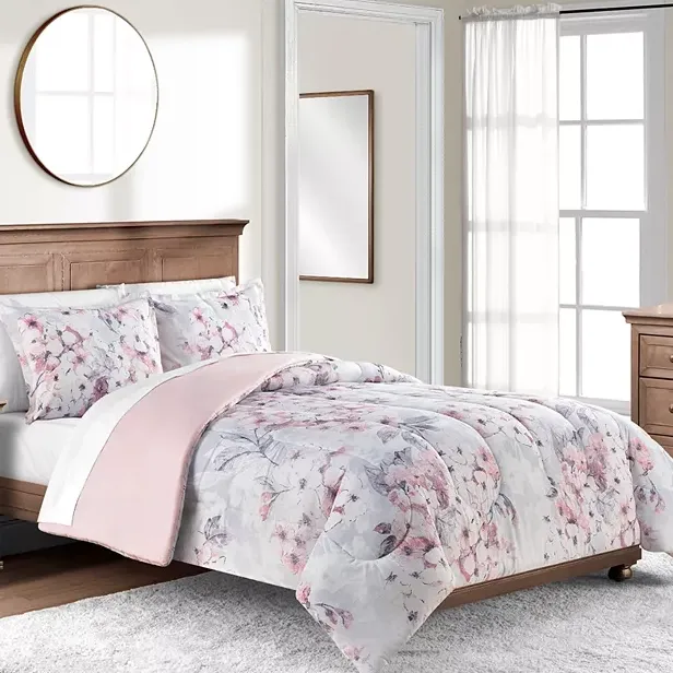 Floral patterned bedding set with matching pillowcases on a wooden bed frame, accompanied by white sheer curtains and wooden furniture.