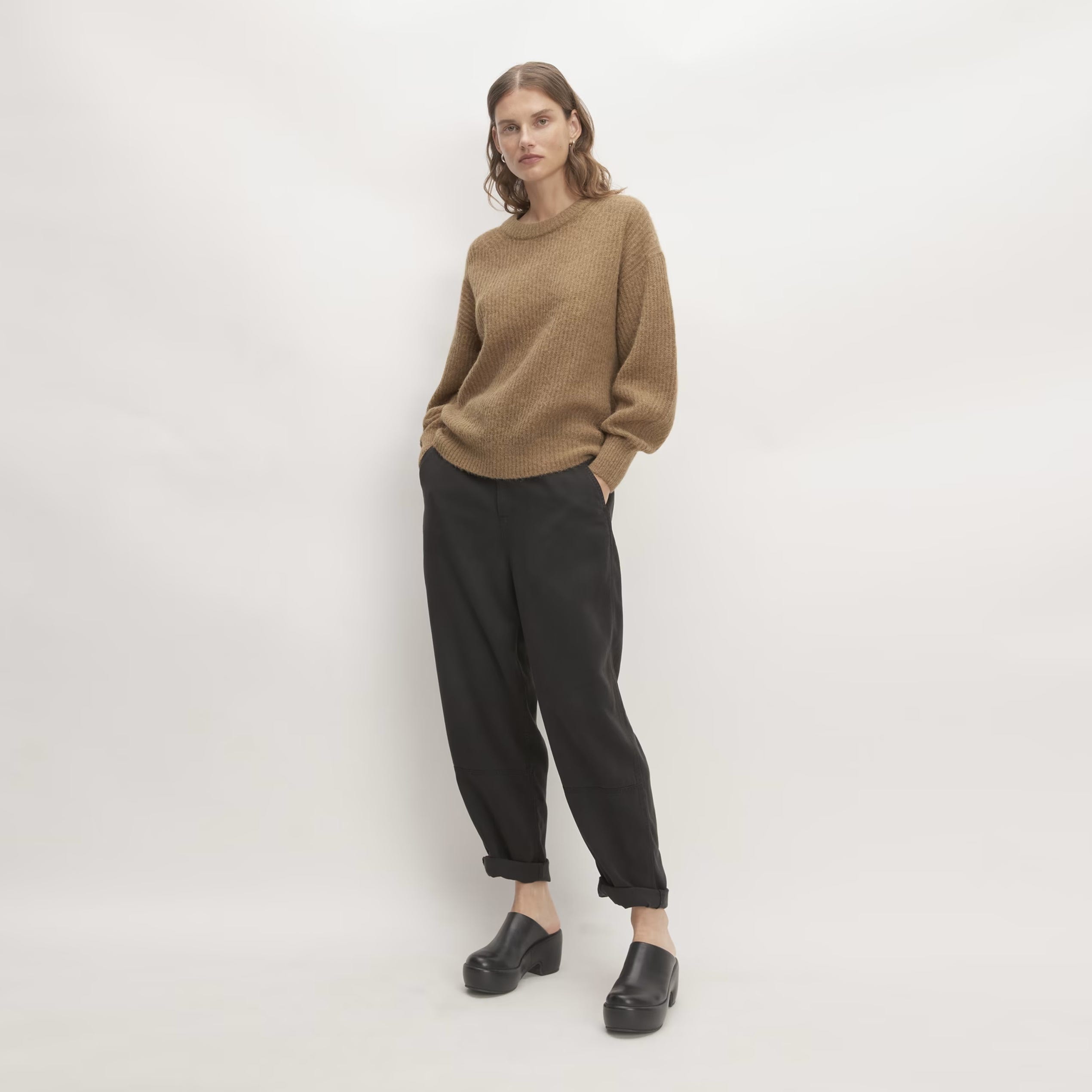 A woman is wearing a camel-colored sweater, black trousers, and black shoes.