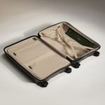 Open Antler luggage with a beige interior, elastic cross-ribbons, a zipper compartment, and a green label.