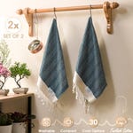 Two blue and white Turkish hand towels with a herringbone pattern and fringe detailing, hanging on a wooden rack.