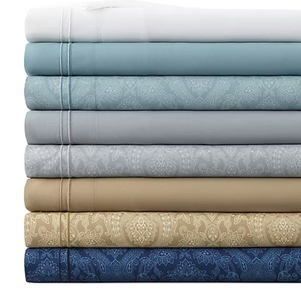 A stack of folded, patterned bed sheets in various colors, including white, blue, gray, green, and beige.