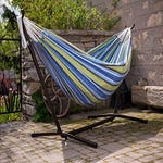 Striped double hammock attached to a curved black metal stand, set on a stone-paved outdoor area.