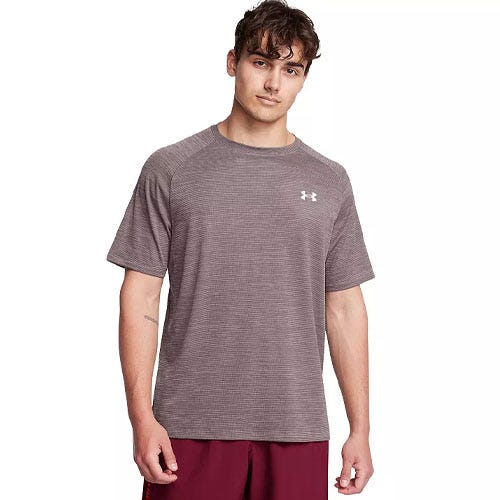 A man wearing a short-sleeve, fitted Under Armour T-shirt with a subtle textured pattern, featuring the brand's logo on the chest. The shirt is paired with maroon athletic shorts.
