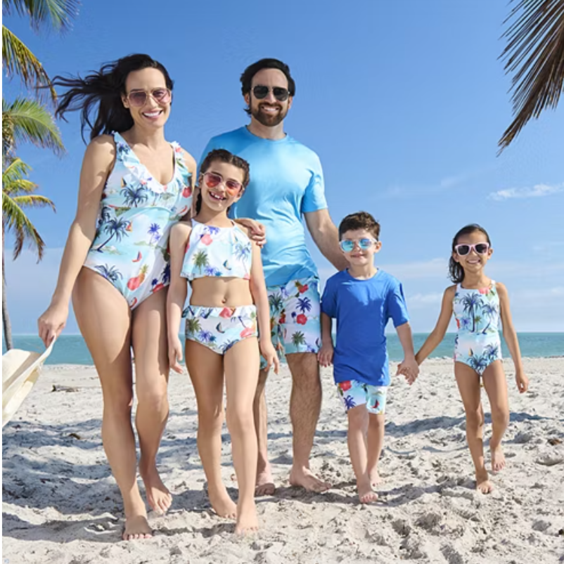 A family wearing matching beachwear with a tropical print, including swimsuits for the women and children and a swim shirt for the man.