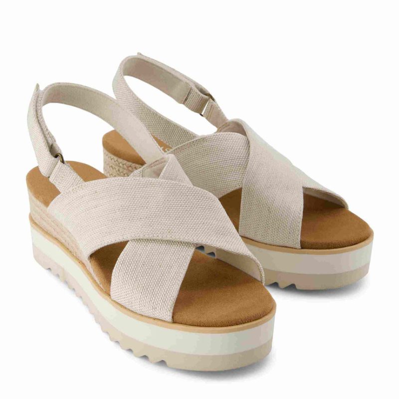 Beige crossover wedge sandals with adjustable ankle straps, a padded brown footbed, and a textured platform sole.