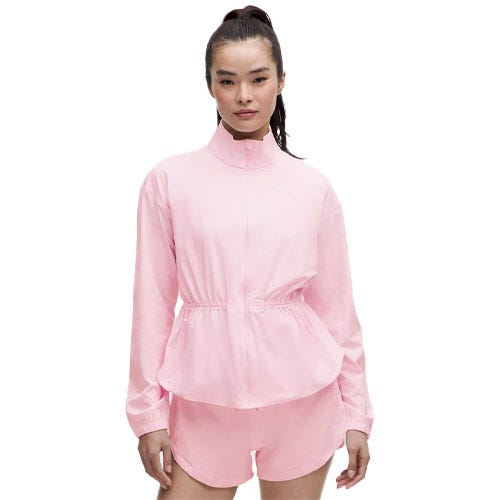 A woman is wearing a pink athletic outfit consisting of a long-sleeve jacket with a drawstring waist and matching shorts.