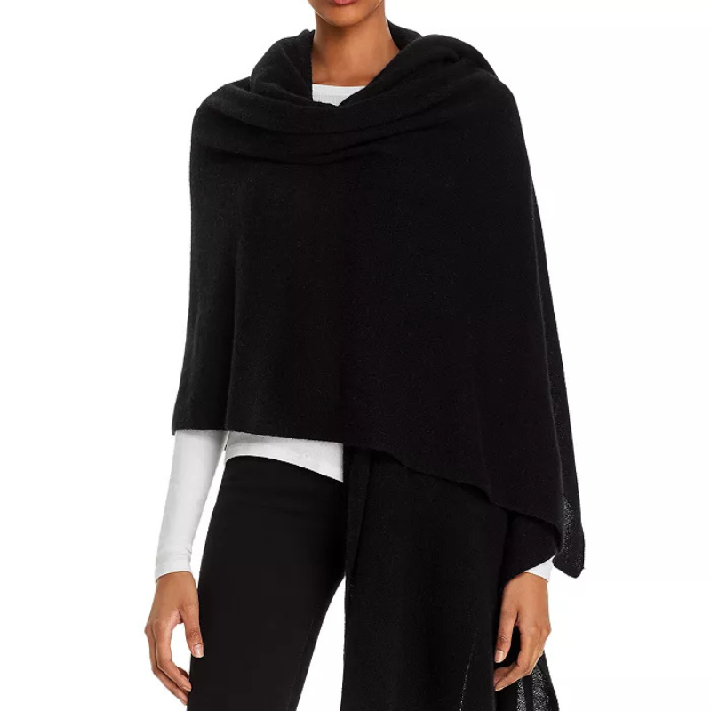 A black cashmere wrap drapes over the shoulders and extends in length, worn over a white shirt and paired with black pants.