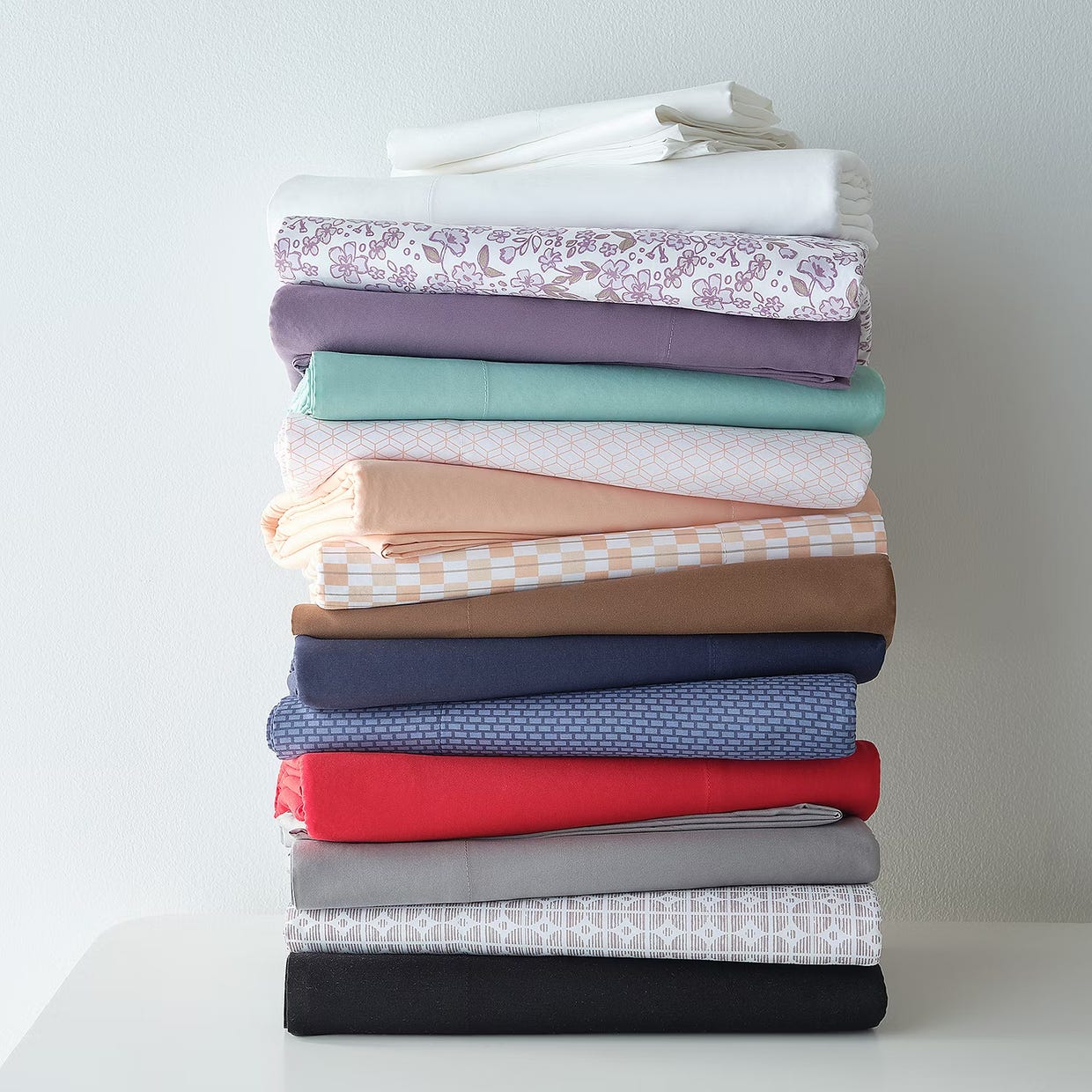 A stack of neatly folded fabrics in various colors and patterns on a white surface.