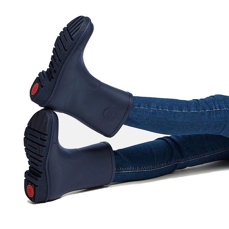 FitFlop WonderWelly Short Rain Boots in navy feature a sleek, modern design with sturdy soles for grip; ideal for wet weather. They're paired with fitted jeans, highlighting their casual style.