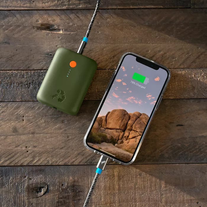 A portable green power bank is connected to a smartphone with a charging indication on its screen.