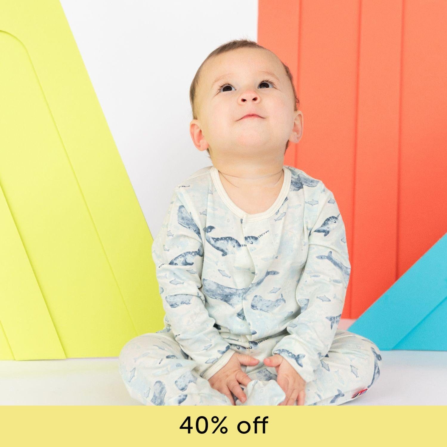 A baby in a blue fish-patterned MagneticMe Footie, looking upwards, with a text overlay indicating a 40% discount.