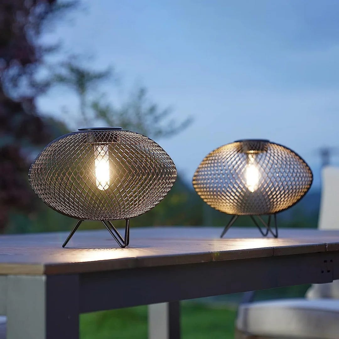 Two spherical metal mesh table lamps with interior light bulbs, set on an outdoor surface at dusk.