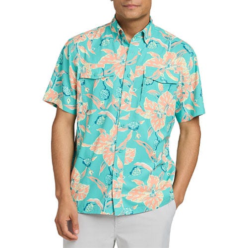 A man is wearing a turquoise short-sleeve shirt with a pink and orange floral pattern, paired with light gray pants.