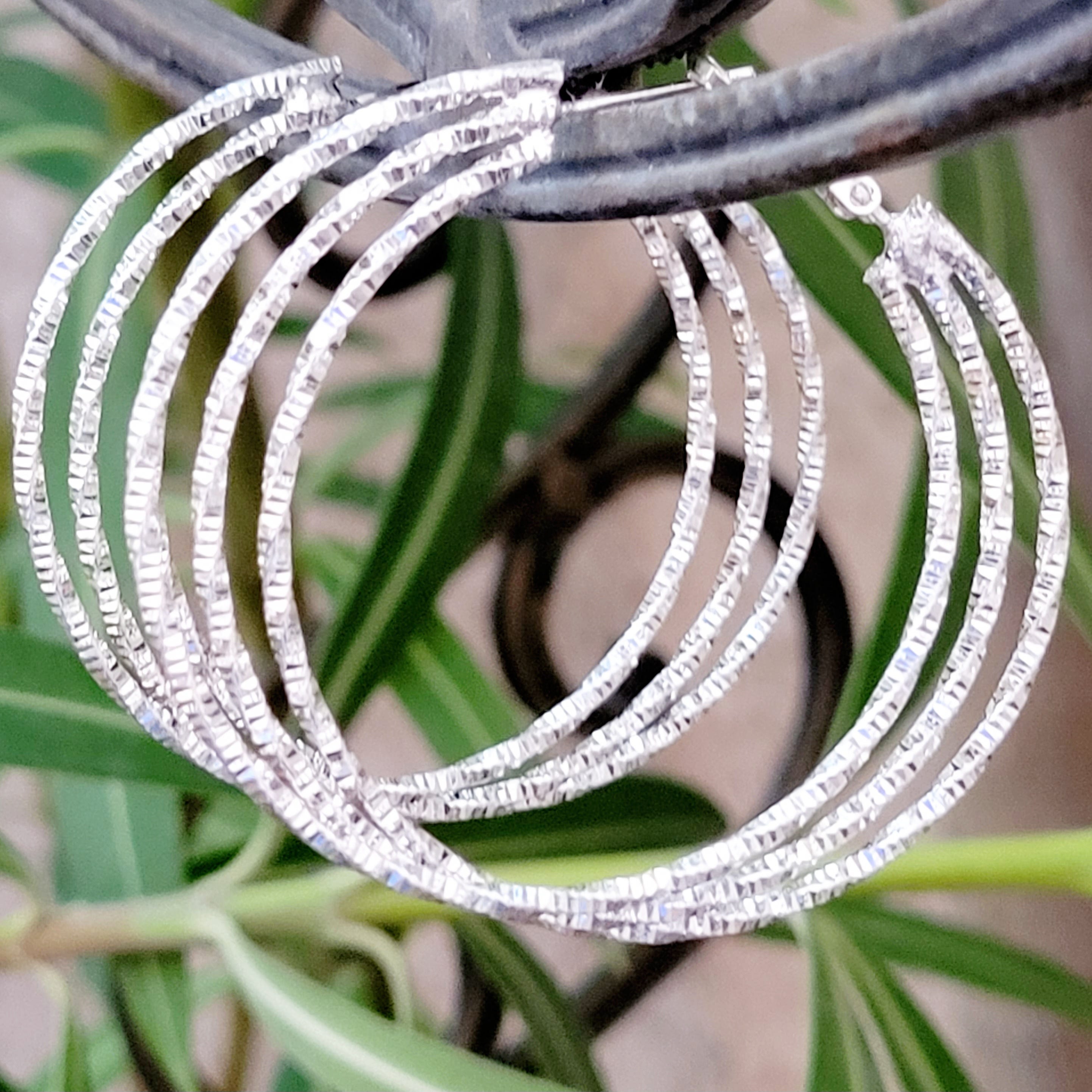 Silver hoop earrings with textured detail, hanging against a green plant background.