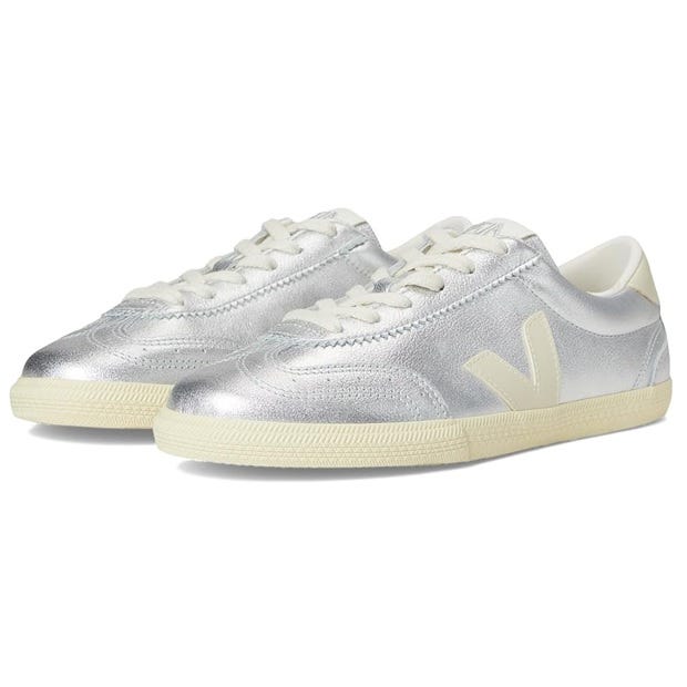 Veja Volley shoes feature a metallic silver upper with a classic low-top design and white laces. They have a beige sole and a distinct \“V\“ logo on the sides.
