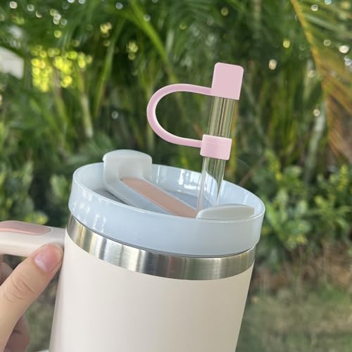 A pink silicone straw topper in the shape of a heart is attached to a clear straw, which is inserted into a tumbler with a white and silver design.