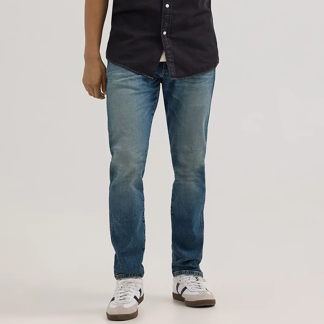 A person is wearing a black button-up shirt, faded blue jeans, and grey sneakers with white accents.