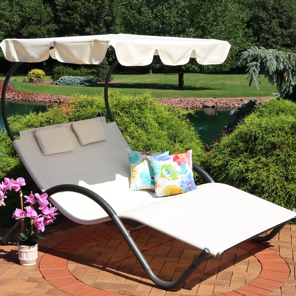 Outdoor double chaise lounge with canopy and decorative cushions set in a garden.
