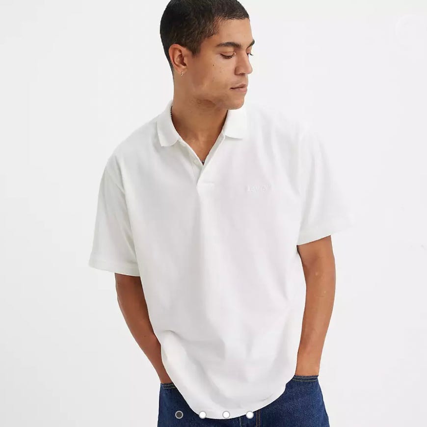 A man is wearing a white polo shirt with a small logo on the chest and blue jeans.