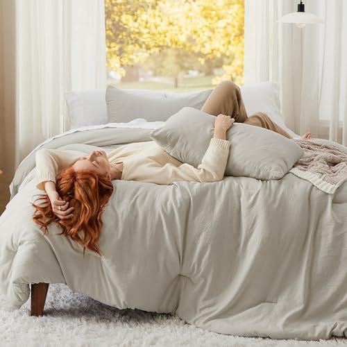 A comforter set featuring a soft-washed finish in a gentle beige tone, paired with matching pillows, adorns a bed in a bright room.