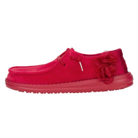 Hey Dude Wendy Velvet Rosette is a vibrant pink shoe featuring a velvet texture, classic moccasin shape, and decorative rosette on the side, offering a blend of casual style and comfort.