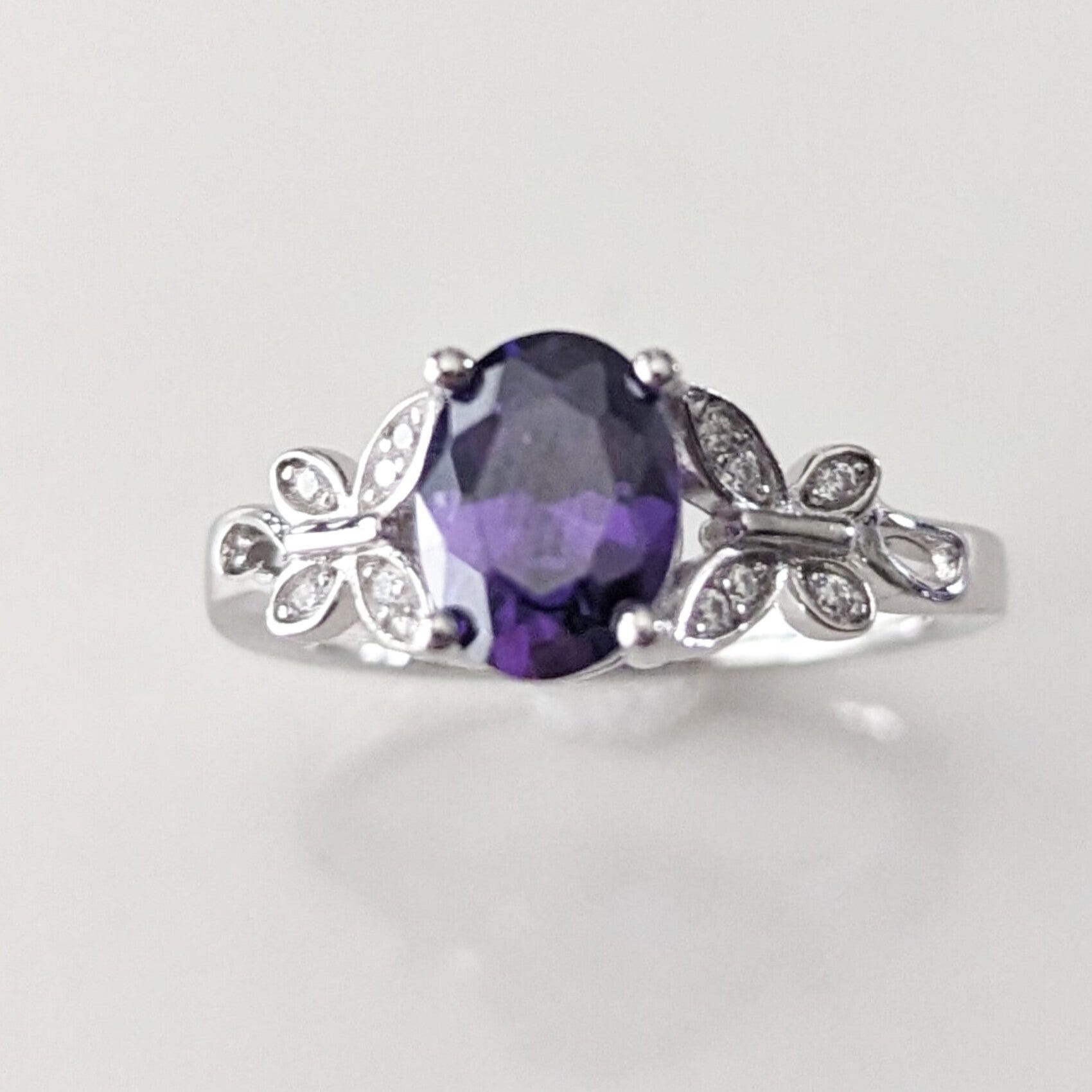 A sterling silver ring with a central oval-cut purple gemstone flanked by two butterfly designs set with small clear stones on the wings.