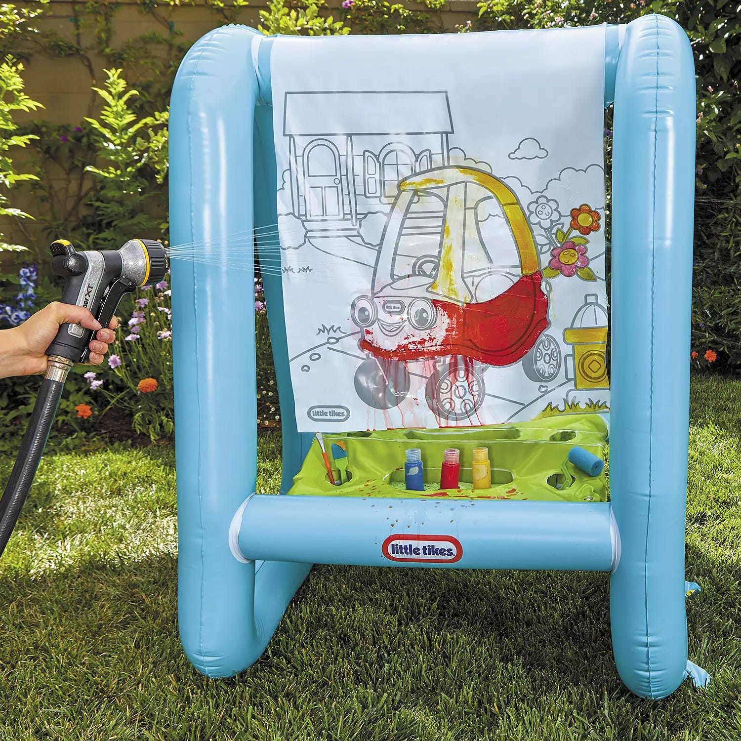 An inflatable easel with a partially colored canvas and paint containers, being hosed down for cleaning.